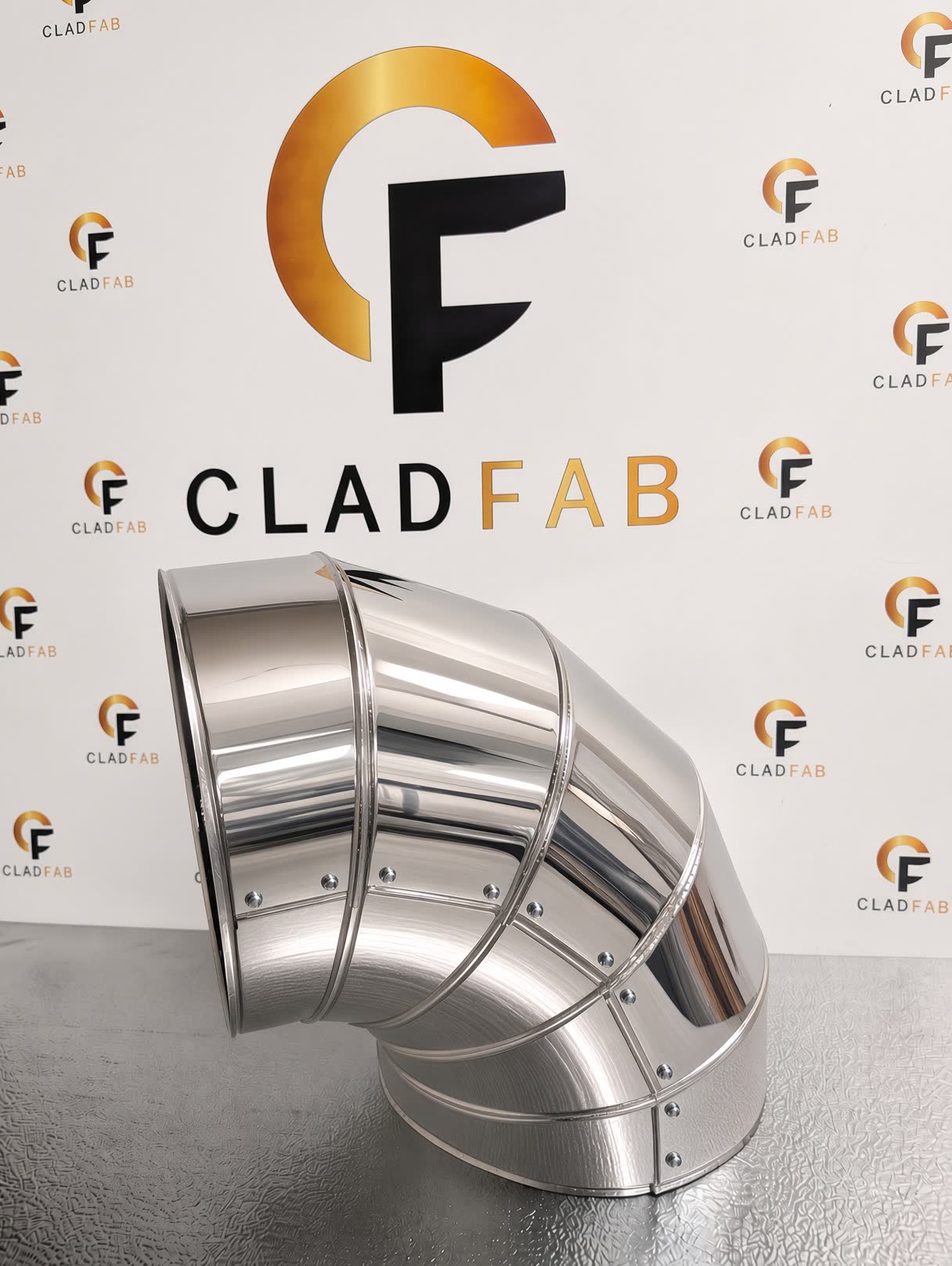 A mirror-polished lobster bend made by CladFab, against the CladFab backdrop