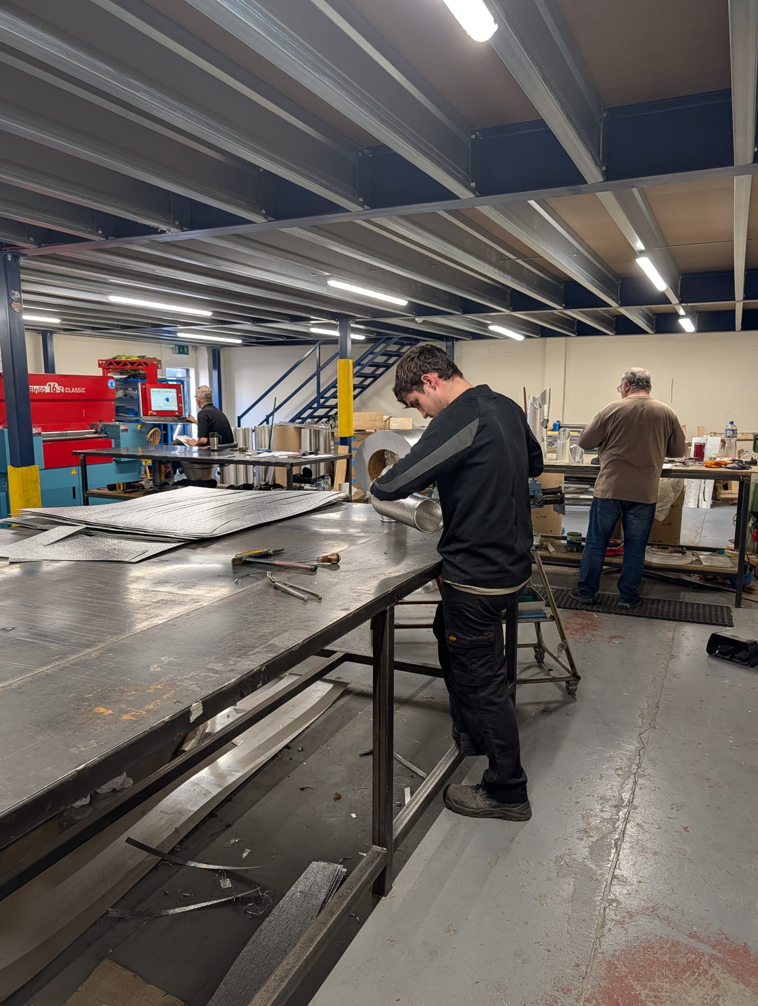 A CladFab fitter forming an aluminium cylinder at the bench, with the MABI line behind